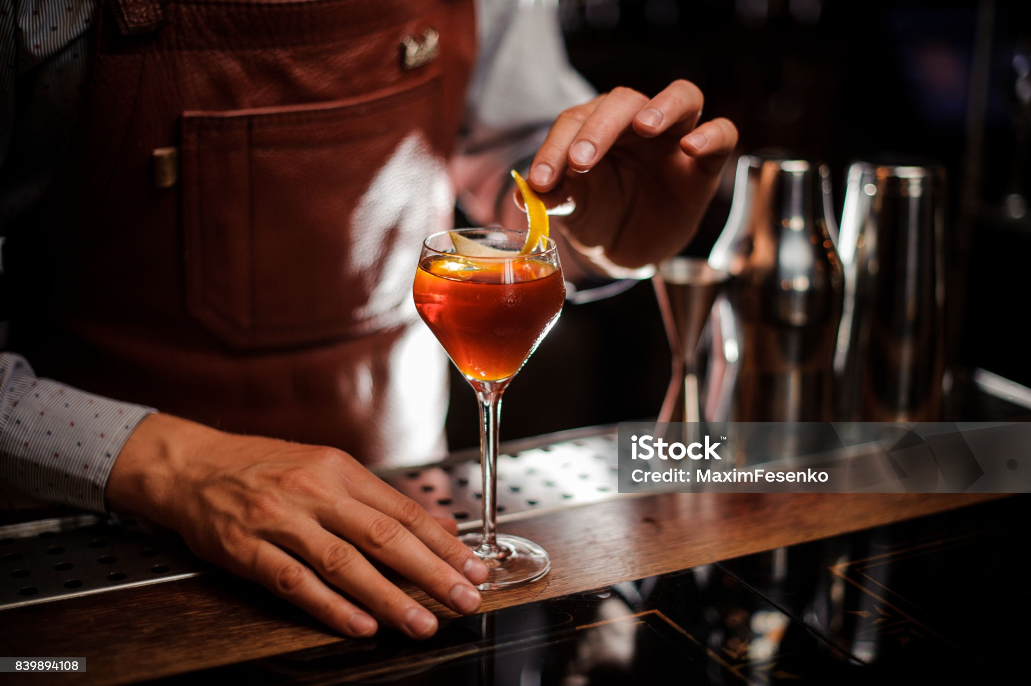 alcohol drinks, people and luxury concept - bartender with glass and lemon peel preparing cocktail at bar